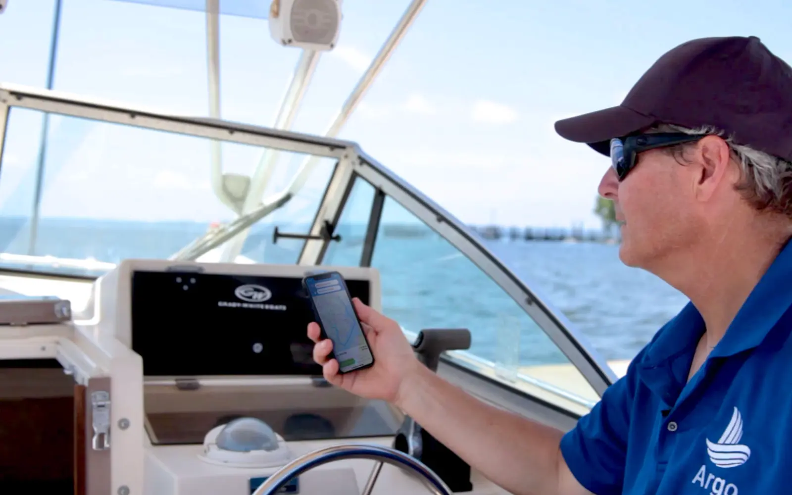 A boat captain at the helm uses the Argo navigation app on his smartphone while cruising on open water.